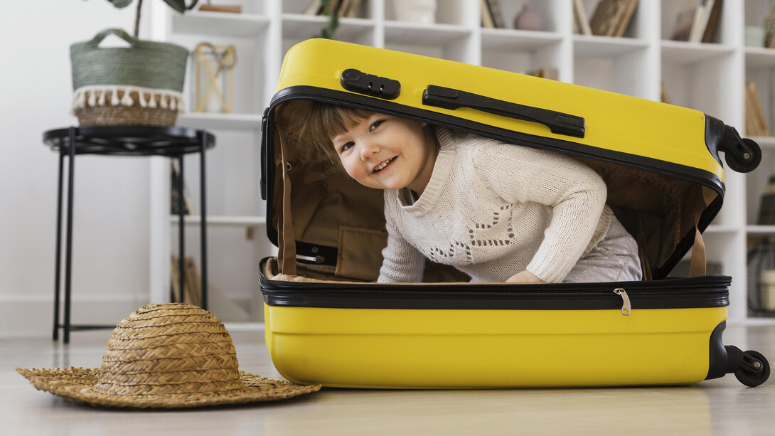 Smiling toddler sitting playfully inside an open suitcase