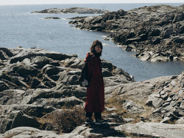 A woman in a long coat gazing out from a rocky seashore, embracing a reflective, in-between moment of change