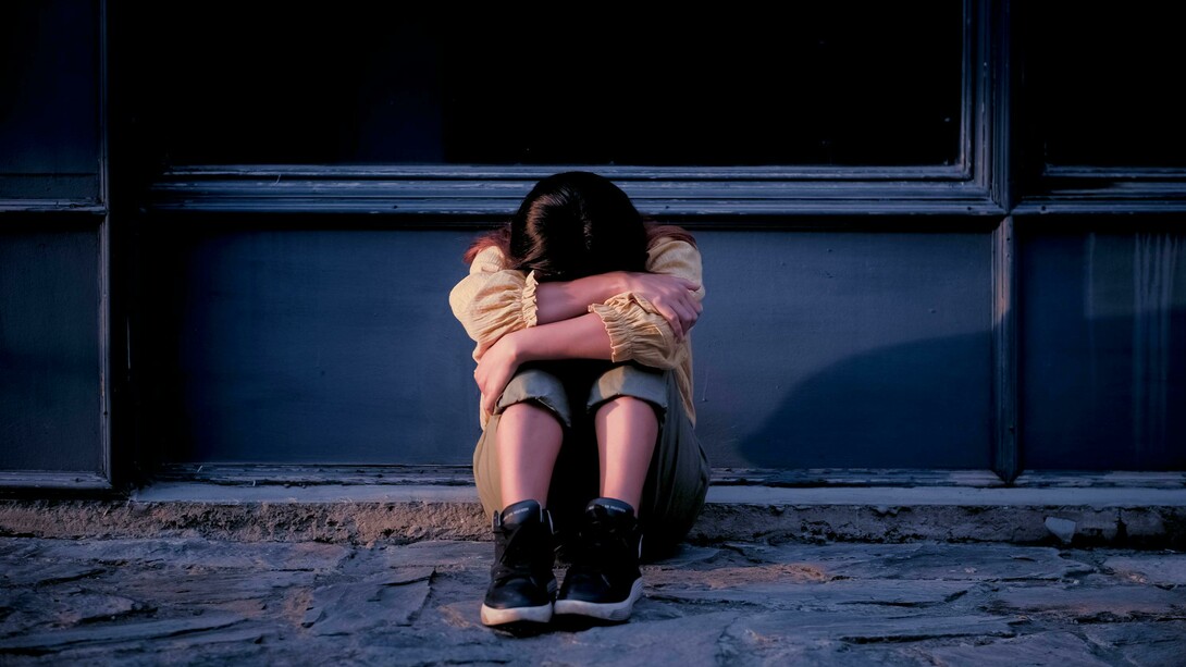 Woman sitting beside a gray wall, looking upset and depressed
