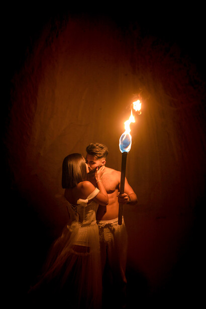 A forbidden embrace unfolds as a couple kisses in the flickering glow of torchlight deep within a secluded cave
