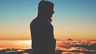 Silueta de una mujer con capucha frente a un idílico atardecer