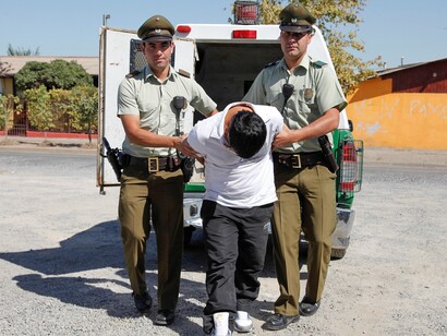 Dos carabineros de Chile escoltan a un detenido