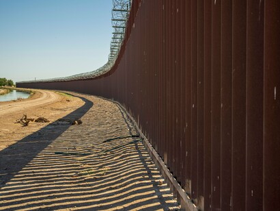 A border barrier casting long shadows across the ground, symbolizing the shifting priorities of modern governments
