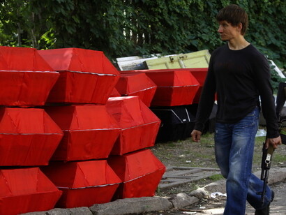 A gunman walks by coffins prepared for the funerals of anti-goverment rebels - Yannis Behrakis