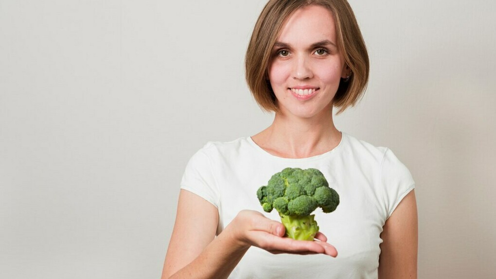 A woman holding a fresh broccoli, emphasizing healthy plant-based nutrition