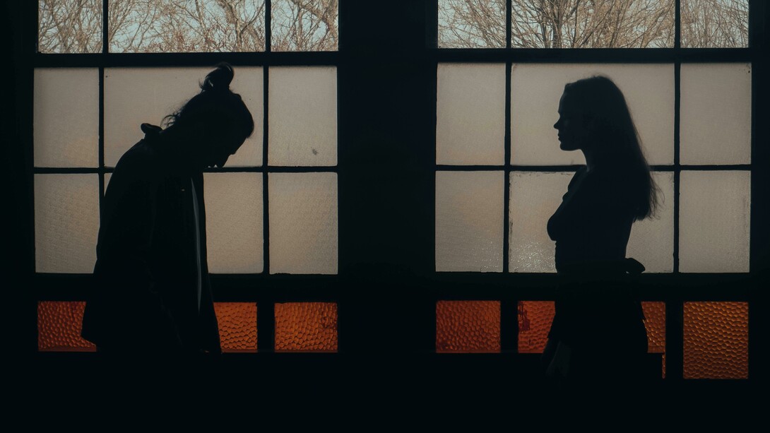 A man and woman standing in a dimly lit room, surrounded by darkness and emotional tension