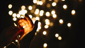 A hand holding a small light against a backdrop of little lights, weaker than a single illuminating focus, but plural and decentralized