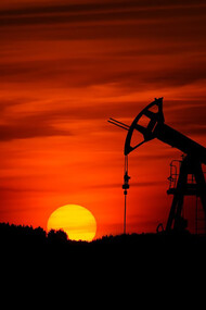 A pump jack extracting crude oil against the backdrop of a sunset