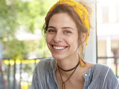 Primo piano di una giovane donna sorridente. L'espressione è gioiosa e serena, in un ambiente luminoso e all'aperto