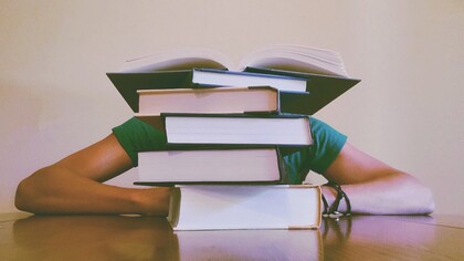 Boy covered up by a pile of books, sometimes the stress of having to study for exams or tests comes up