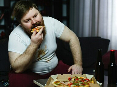 Sitting on the sofa, a man flips through TV channels while snacking on unhealthy foods, reflecting a sedentary lifestyle