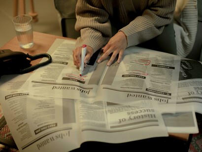 A close-up shows a woman looking through job advertisements, capturing the quiet reality of post-graduation job searching