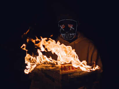 A man in a mask holds a newspaper on fire