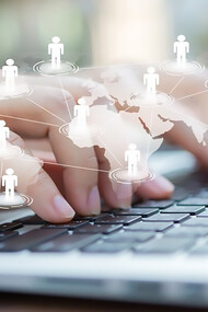 Hands typing on a laptop, with a virtual world map in the background, symbolize virtual interaction, social connection, and the power of digital communication