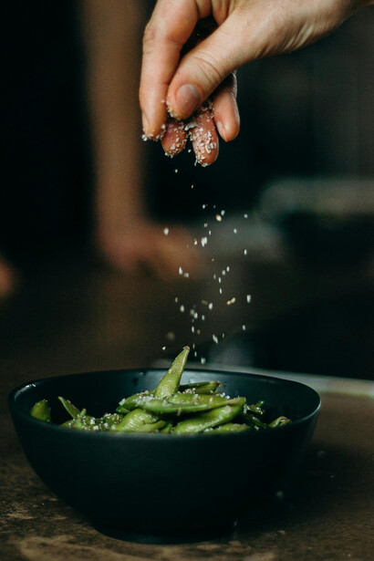 A close-up of sweet peas being stir-fried and salt poured over green beans, highlighting nutritious vegan snacks