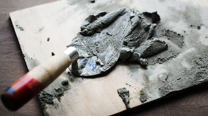 Una cazzuola da muratore appoggiata su un pezzo di legno, con sopra un mucchio di cemento o malta fresca, pronta per l'uso