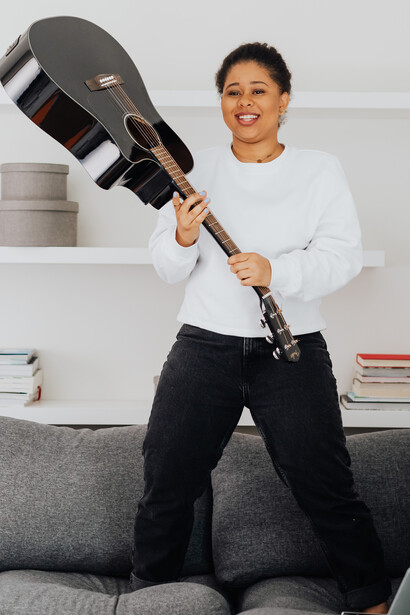 Mulher toca violão feliz em cima do sofá