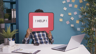 A worker raising a “HELP!” message while seated at a computer, symbolizing how a need for assistance can become an opening for social engineering