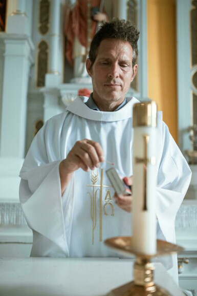 Inside the church, a priest prays as he lights a candle