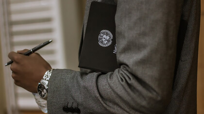 A man holding a black book with the UN emblem on it and a pen, symbolizing diplomatic and administrative work within the United Nations