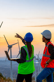 A team of young maintenance engineers works at a wind turbine farm at sunset, inspecting and maintaining the equipment