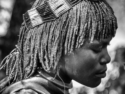 Mulher da tribo Hamar, na Etiópia. No meu segundo dia, Asu me convidou para acompanhar um ritual tradicional da tribo Hamar, no qual um jovem se transforma em homem. O ritual envolve várias etapas e testes de coragem, sendo um dos mais icônicos o famoso salto sobre as costas de vacas, realizado completamente nu. Mas, antes disso, ocorre um momento marcante: o chefe da tribo começa a chicotear as mulheres, que se colocam voluntariamente para demonstrar sua força e coragem. Elas disputam entre si para ser as escolhidas, como uma forma de apoiar o jovem que está passando pelo rito de iniciação