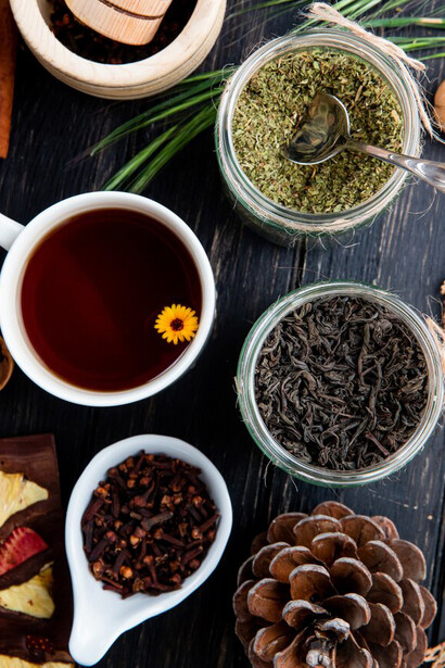 A top view showcasing a variety of dried spices and herbs, such as black tea leaves, peppermint, rose, and Ayurvedic herbs