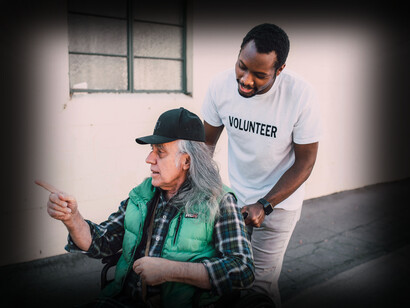 Um voluntário transporta um idoso em cadeira de rodas