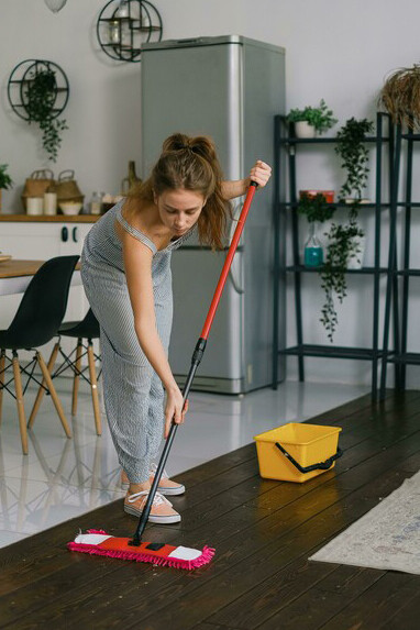 A tired woman mops the floor in her home, reflecting the strain of daily chore
