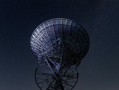 A large radio telescope dish points toward the night sky, representing the type of radar and signal-tracking technology used to detect unknown objects