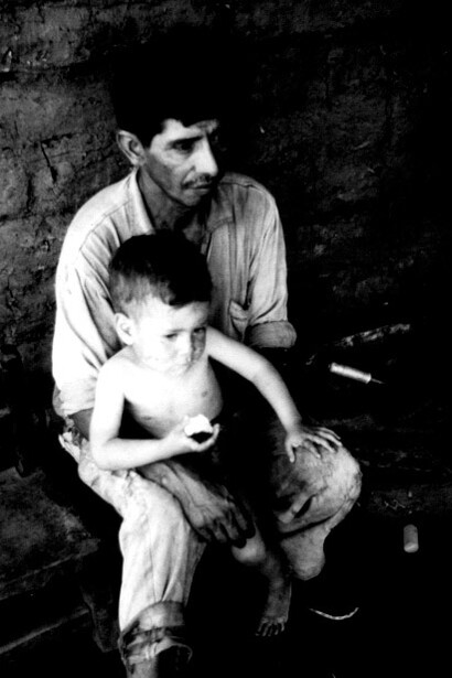 Trabajador de la industria azucarera con un niño descalzo dentro de una vivienda de adobe. Tucumán, Argentina, octubre de 1968