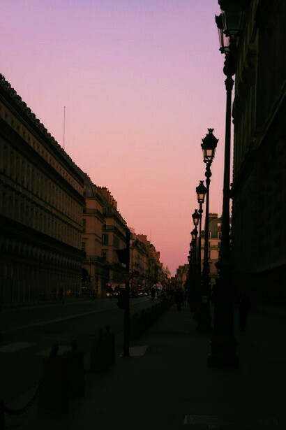A quiet street in Paris at dusk, illuminated by a glowing streetlamp beneath pink-tinged clouds, France