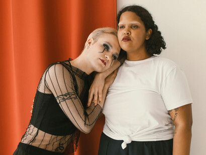 A lesbian couple sharing a quiet moment, one woman in a black dress leaning on her partner in a white shirt
