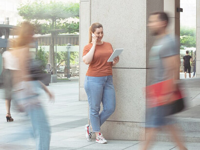 A woman on a bustling street, engrossed in a phone conversation amidst hurried passersby, illustrating the dynamic pace of modern urban life and the omnipresence of time