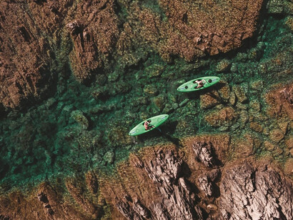 The rugged coastline of Isola Rossa, Sardinia, adorned with red granite cliffs and lush Mediterranean vegetation, creates a striking contrast against the shimmering waters of the Tyrrhenian Sea, Italy