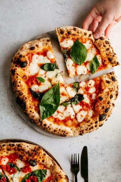 Hands present a pizza, poised for the sacred first bite