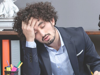 A visibly burnt-out businessman sits at his desk, gripping his head in distress, symbolizing the toll of workplace stress and burnout