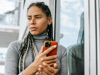 A tired Black woman stands on the street using her smartphone, her face reflecting concern and mental fatigue