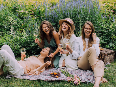 Beneath the sky's expanse, four women sit on the verdant grass, sipping wine and merrily commemorating Galentine's Day, basking in the glow of their enduring friendship