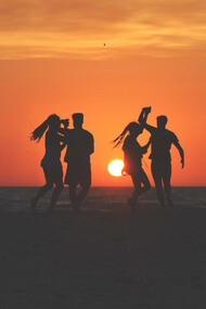 Dos parejas bailando en la playa frente al atardecer