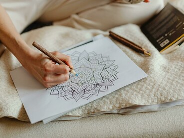 A person coloring a mandala with a colored pen