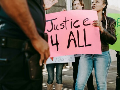 A young woman holding a protest sign in front of a police officer