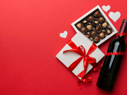 A romantic scene with a bottle of red wine, a heart-shaped box of chocolates, and a beautifully wrapped gift, all set against a colorful backdrop