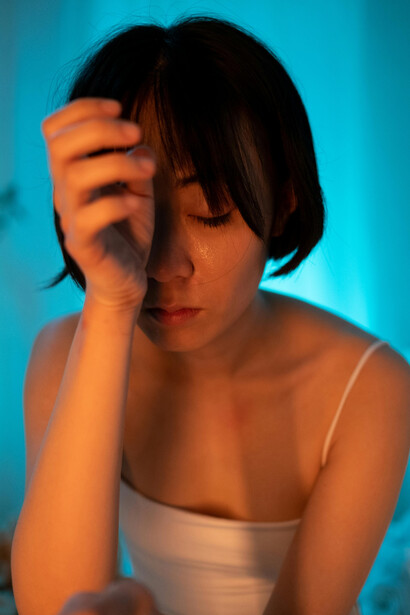 A short-haired woman in a white tank top holds her face in distress