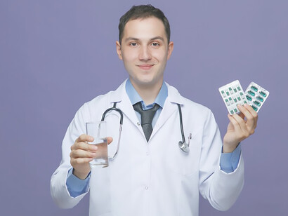 Young male doctor happily holding medication, dressed in medical robe with stethoscope around neck