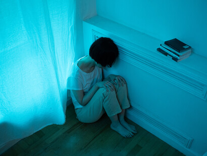 A woman huddles in the corner of her apartment with her head down