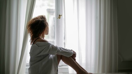 Young woman sitting on a sofa at home, looking out the window