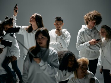 Um grupo diverso de pessoas, vestido de branco, utiliza smartphones e um bastão de selfie. A repetição de gestos e dispositivos evidencia a presença dos mesmos hábitos de comunicação digital, que podem ser explorados para difundir mensagens políticas e reforçar visões de mundo semelhantes