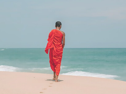 A person dressed in Buddhist attire stands by the seashore