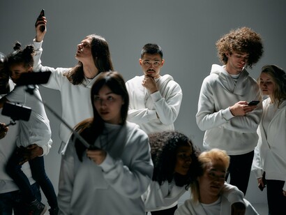 Um grupo diverso de pessoas, vestido de branco, utiliza smartphones e um bastão de selfie. A repetição de gestos e dispositivos evidencia a presença dos mesmos hábitos de comunicação digital, que podem ser explorados para difundir mensagens políticas e reforçar visões de mundo semelhantes